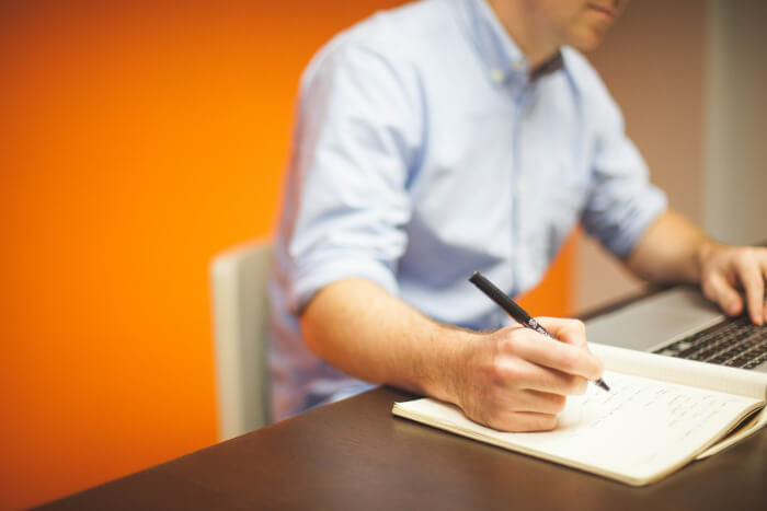 man taking notes while looking at his laptop screen