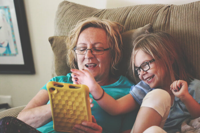 adult looking at a tablet with a child looking as well seating on a couch