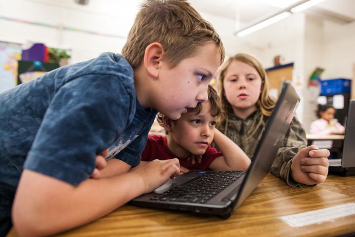 Boy leaning over computer with two kids in the background