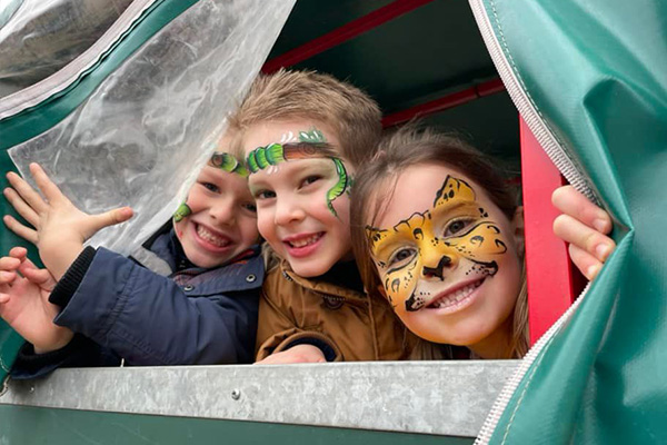 Three children with face-paint on peering out the side of a farm tractor on one of Hall Farm's tractor trailer rides