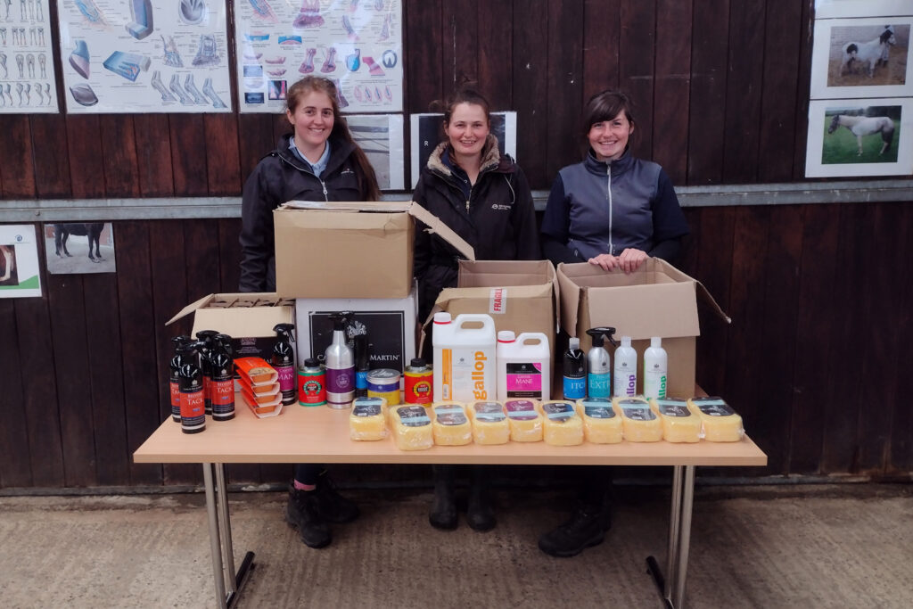 Three World Horse Welfare grooms stood behind a table full of donated Carr and Day and Martin products