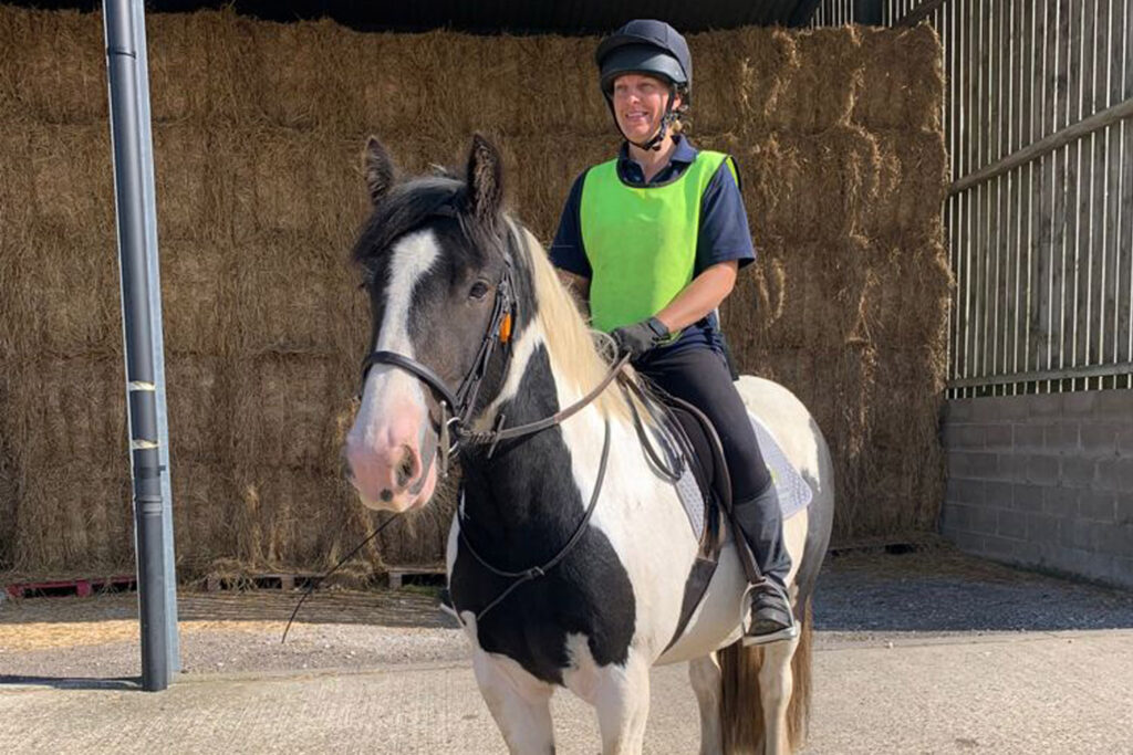 Piebald cob stood in yard with rider wearing high vis 