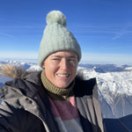 Lady wearing woolly hat stood at top of mountain with snowy mountains in background