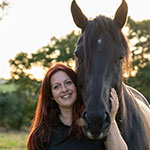 Jenny Rogers standing close to a black horse in a field with her hand on the horse's face