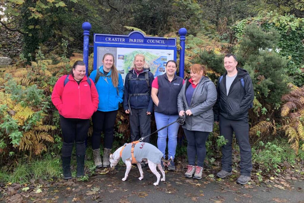 A group of six walkers and one dog pose by a sign in Craster, Northumberland ahead of their sponsored 15-mile walk for World Horse Welfare along the Northumberland Coastal Path.