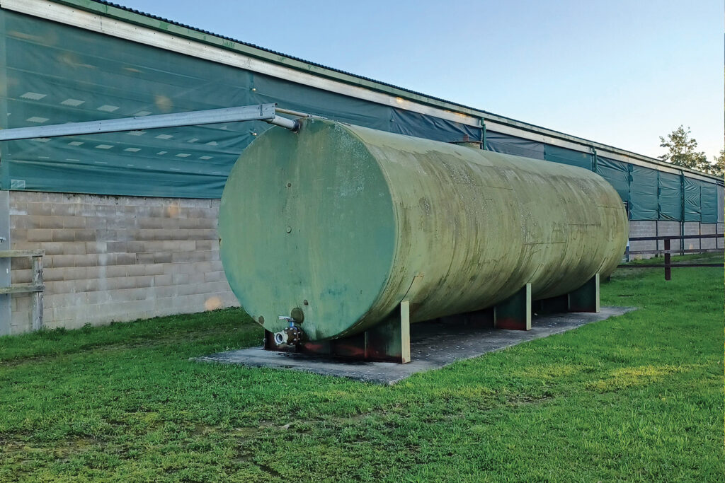 A large green water tanker next to an indoor riding arena.