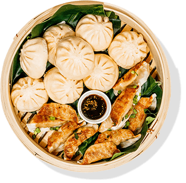 bao and potstickers with dipping sauce in a large steamer basket