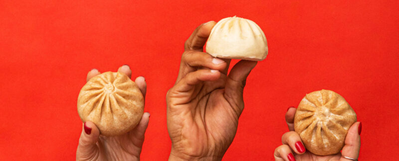 Three hands, each holding up a bao. 2 of them, are whole wheat vegetable bao.