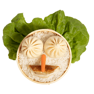 The lil bunz kids meal. A steamer basket filled with rice, and sitting on top are 2 bao, one potsticker, and one carrot, arranged to look like a face. There is a piece of lettuce behind the food to look like hair.