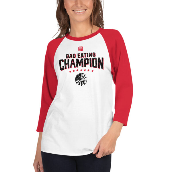 A female presenting person wearing a 3 quarter red sleeve baseball tee, saying "BAO EATING CHAMPION" in large font with stars and a grunge-y bao illustration below it