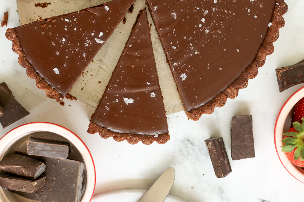 Sliced Gluten Free Chocolate Ganache Tart with pieces of dark chocolate scattered around the tart