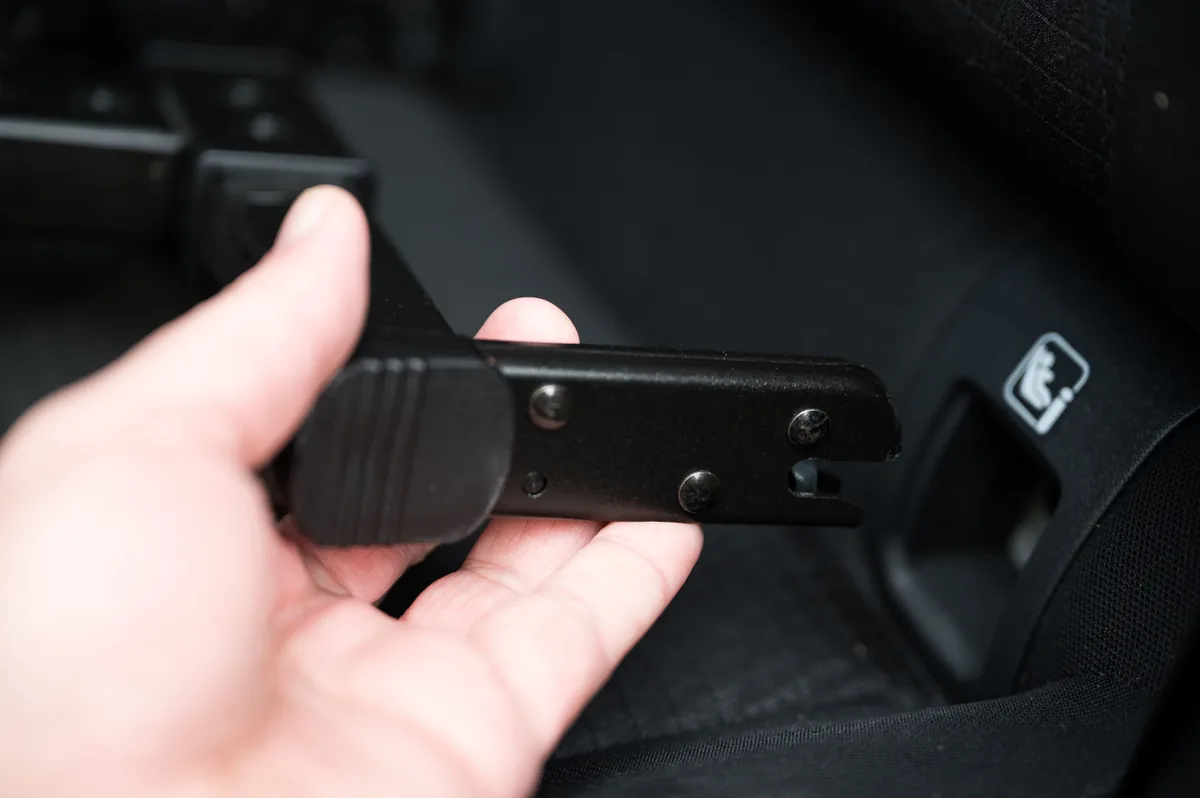 Ruka držící kotvící část autosedačky s Isofixem