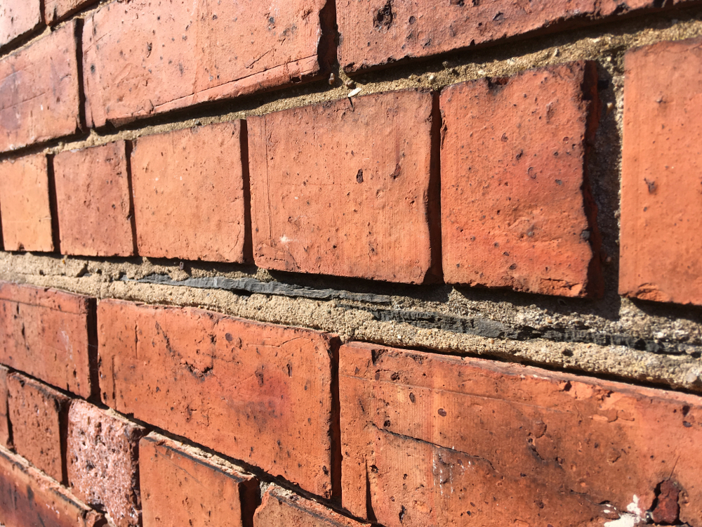 Red brick wall with old fashioned slate damp proofing