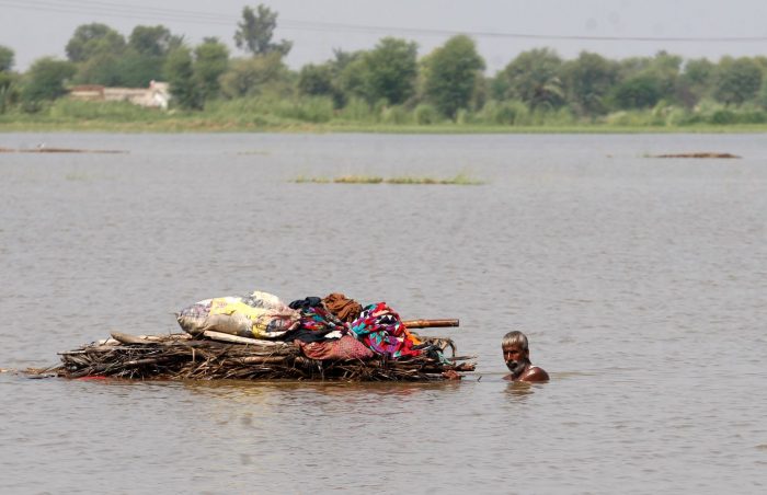 A man wades through deep floodwaters in Punjab, Pakistan with his belongings balanced on a raft.