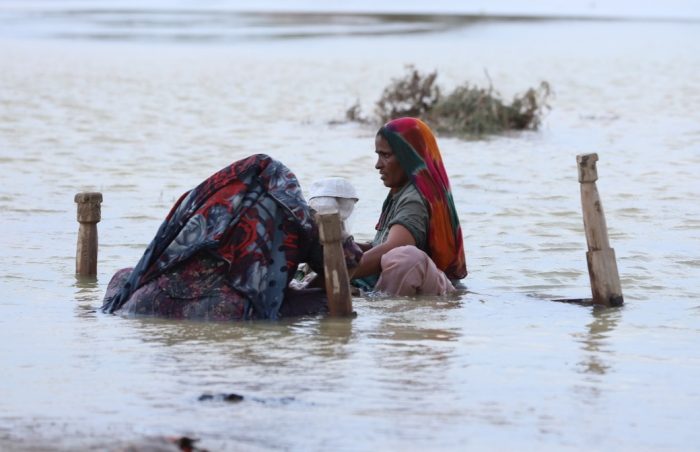 Lady wading through flood waters in southern Punjab, Pakistan with her possessions balanced on an upturned bed.