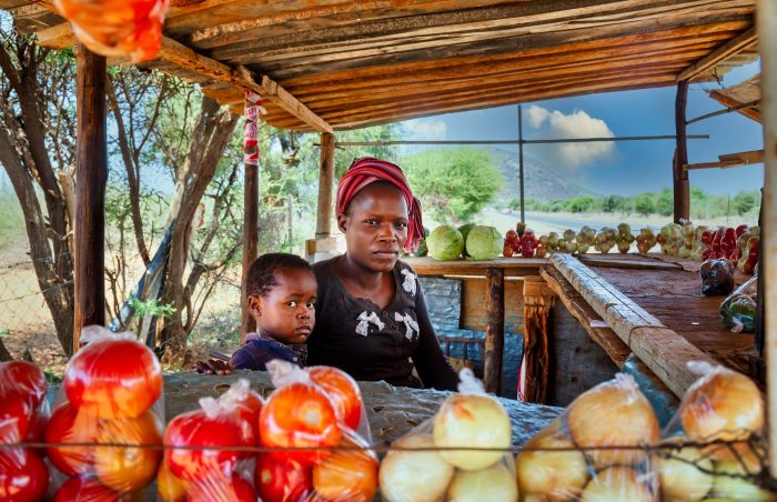 A mother and child in their vegetable stall in Africa that sells, onions, tomatoes and cabbages.