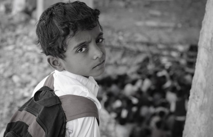 Young schoolboy with a satchel in Taiz, Yemen, looking back.