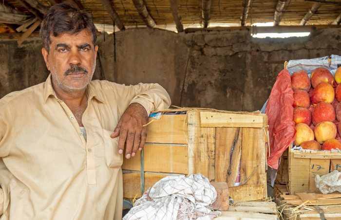 A fruit vendor in PAkistan stands next to his stall with the produce he has grown in his orchard.