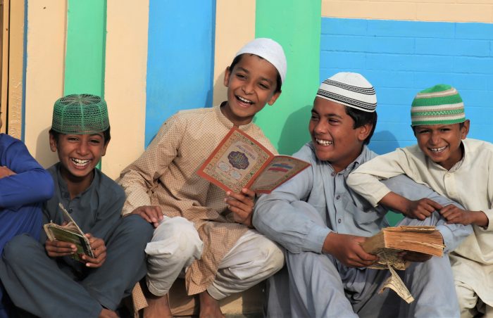 Small mosque in Sindh, Pakistan, showing smiling boys, reading texts.