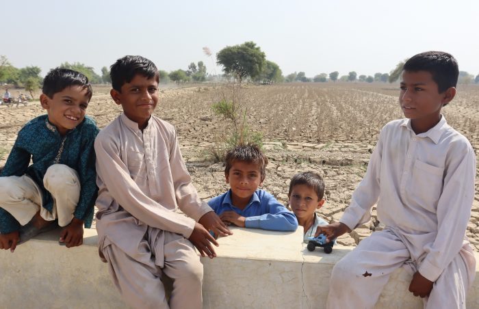 5 smiling and happy boys sitting on the wall in flood affected Rajanpur, Pakistan