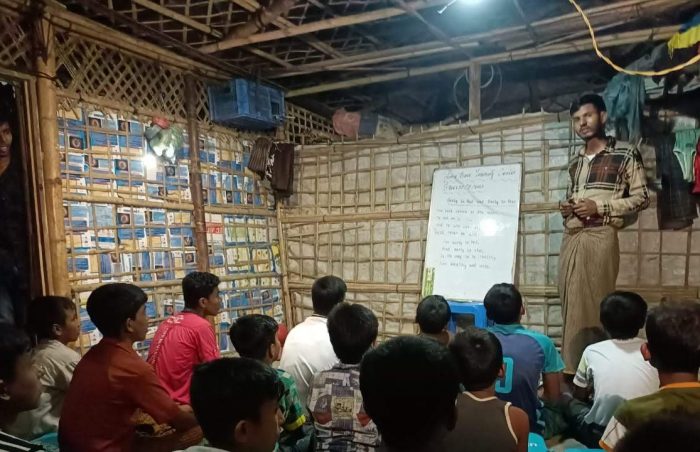 A class of bangladeshi schoolboys sit in class listening to their teacher under a single naked lightbulb