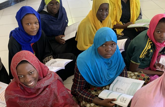 EcoVillage orphan girls reading books sitting on classroom floor in Tanzania.