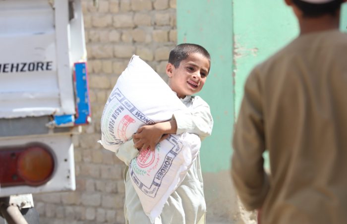 Afghani refugee boy holds onto his sack of wheat as he runs from the truck.