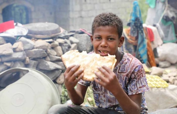 A boy bites into his bread whilst sitting amongst the rubble of his destroyed family home in Yemen.