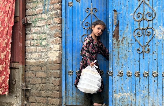 Distribution in Afghanistan, a girl carries cooked prepacked food for family into her home with blue gate
