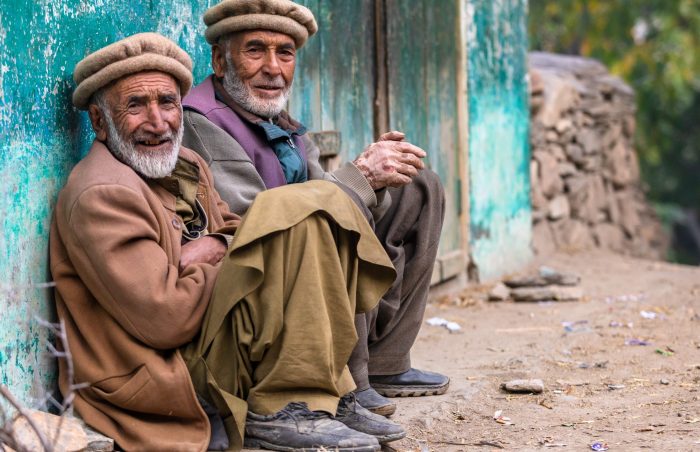 2 smiling and happy old gents sit against a turquoise wall in Northern Pakistan