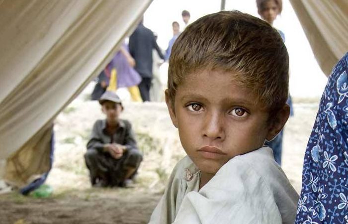 Sad orphan child in a refugee camp tent looks into camera intensely.