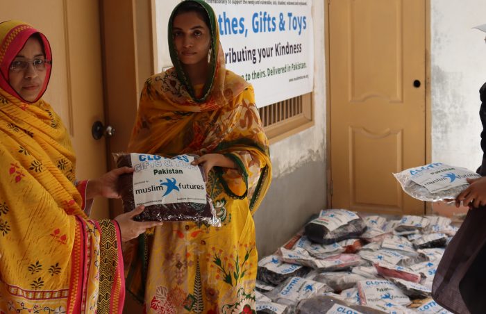 A woman in Pakistan holds onto a packet of good quality donated clothes, with a pile of donated clothes in packets in the background.