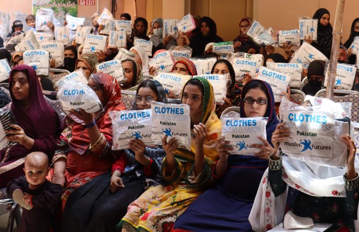 Women and children attend the distribution of the latest Comfort at Home distribution in Pakistan holding high their packets of good quality donated clothes.