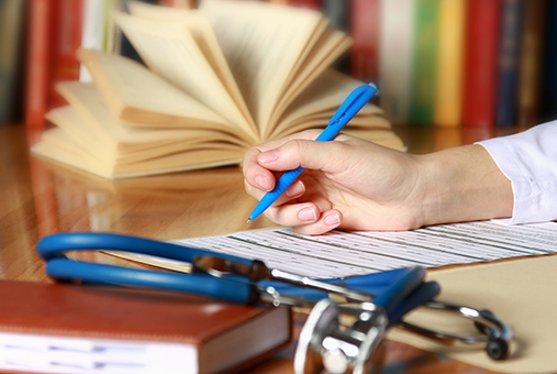 Close-up of writing doctor's hands on a wooden desk