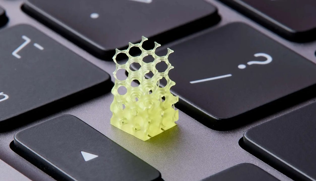A small yellow 3D-printed lattice structure with a hexagonal pattern, placed on a keyboard for scale.