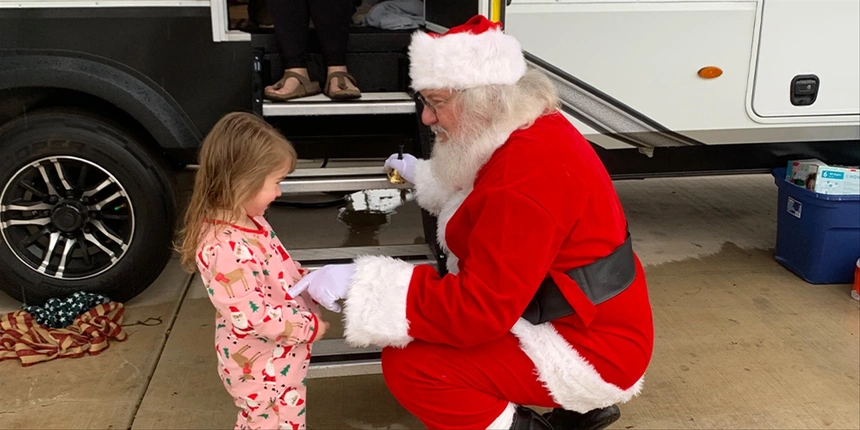 Santa and a girl next to an RV talking. 