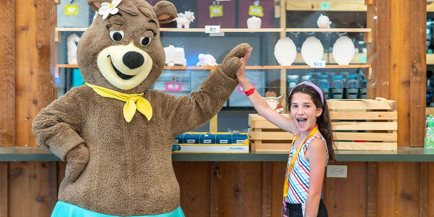 A camper high-fiving Cindy Bear™ in front of the ceramics.