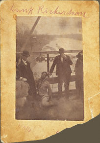 The corpse of Bunk Richardson, propped up for photographer on plank walk of bridge spanning the Coosa River, severely beaten, stripped to long johns. Onlookers hold handkerchiefs to cover nose and mouths.
