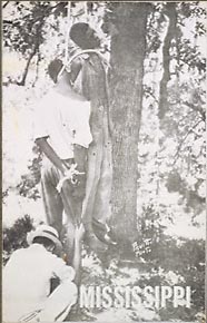 Lynching of two unidentified African American males, white man squatting, hides face as he stills corpses.