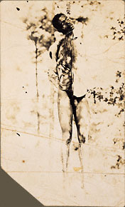 The lynching of unidentified African American male, naked lower body, bloodied, bullet holes.