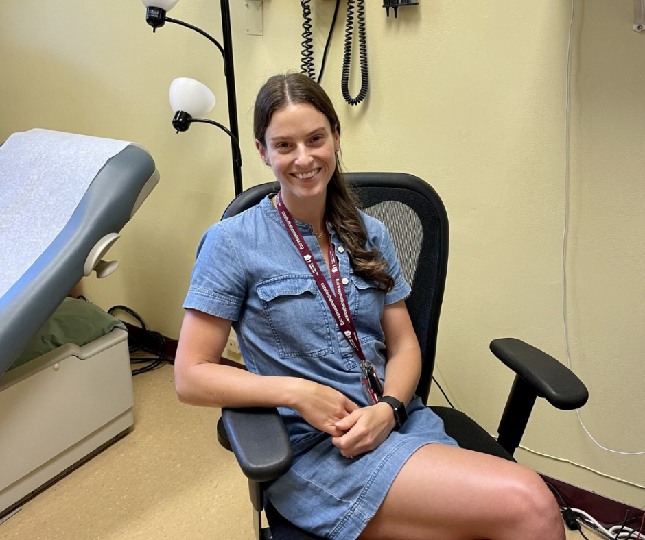 A smiling woman in a nurse's uniform sits in a chair