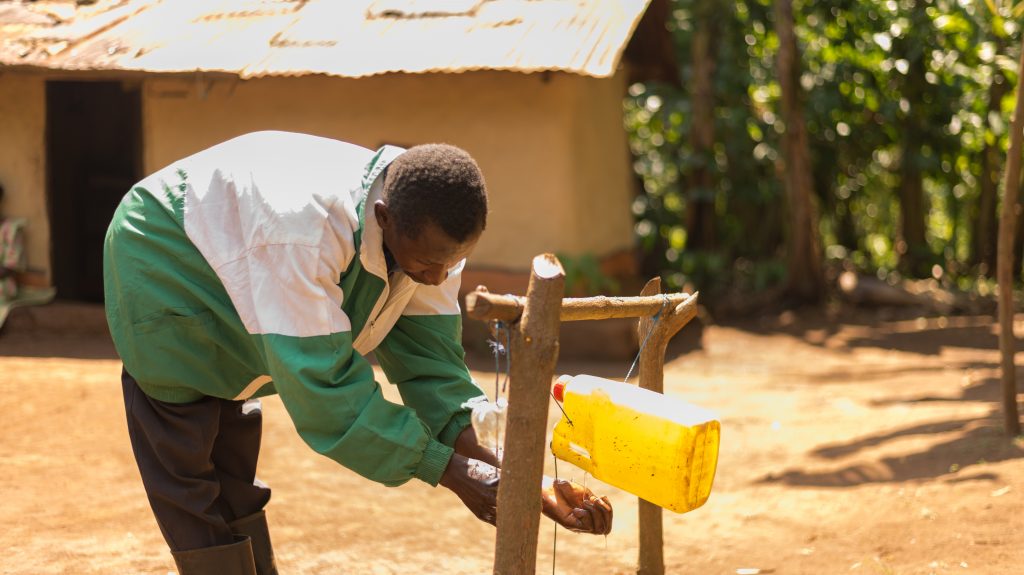 A man washes his hands using a homemade Tippy Tap station