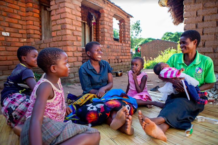 A group of children gather around a Mother Mentor