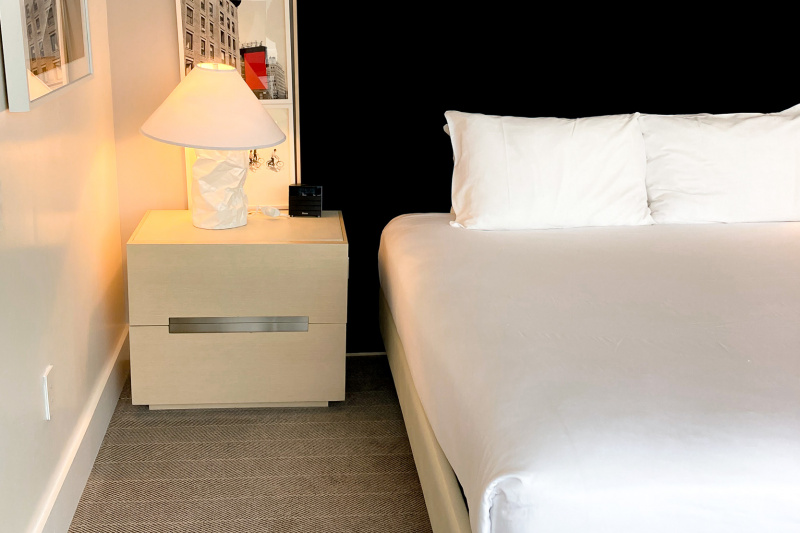 The accessible suite, with space between the side of the bed and the wall, with a bedside table with a lamp.