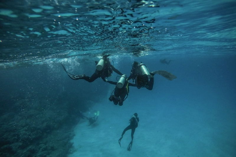 Two divers help another one dive through the Anakena Sea.