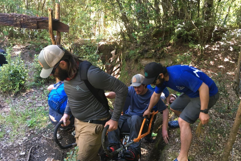 A group of friends travers uneven lands using a joelette wheelchair
