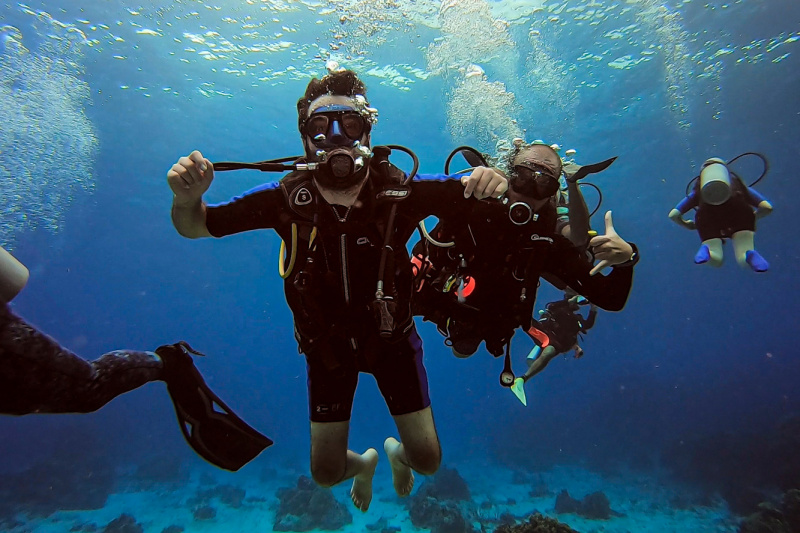 A scuba diver and instructor swim underwater next to Cozumel reef.