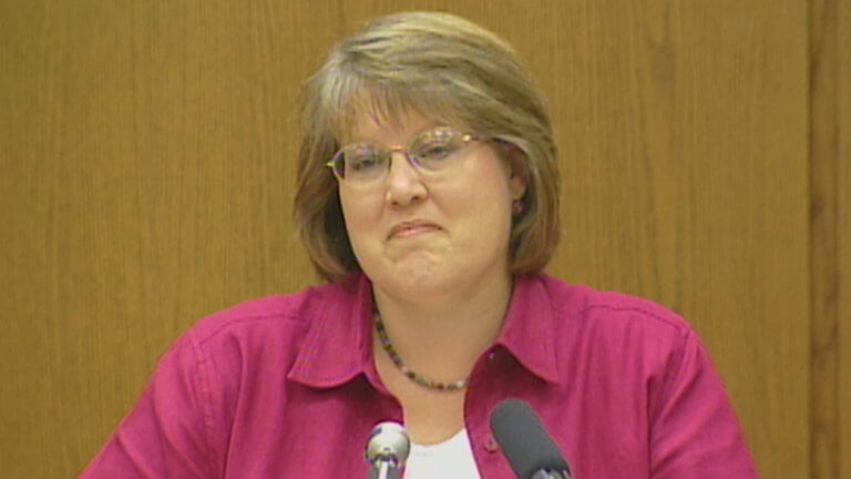 A woman in a red collared shirt testifies
