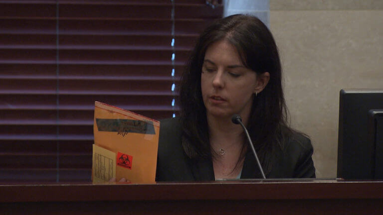 A woman looks at an envelope on the witness stand