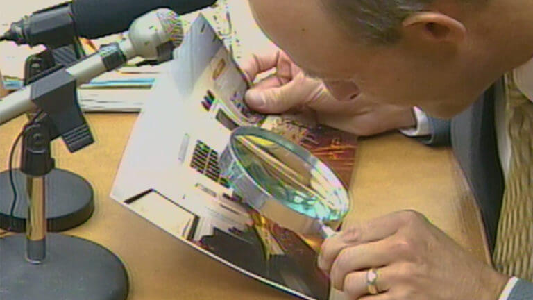 A man looks at a photo through a magnifying glass.